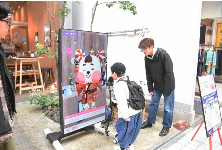 店舗前の大型画面に表示されたAIコンシェルジュと対話する利用者の様子